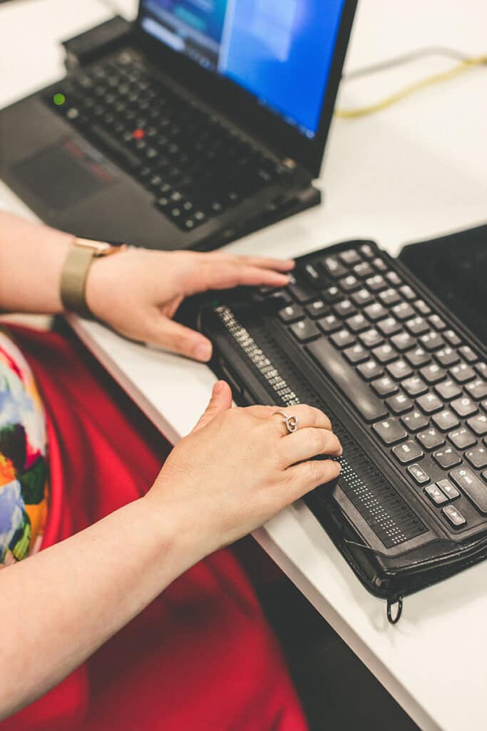 Photo: a woman sits at a desk, using a braille keyboard for accessiblity testing.