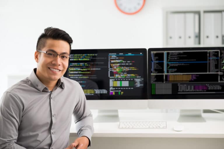 Closeup of an Asian QA engineer in front of his computer screens.