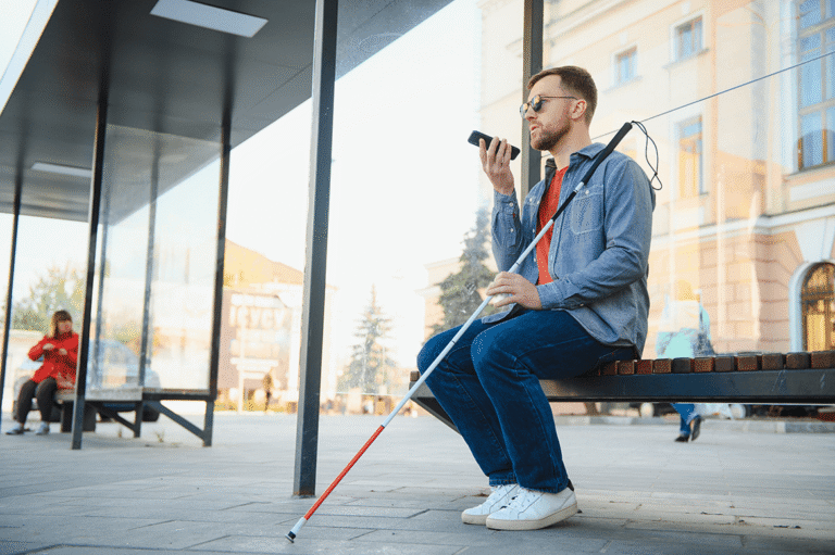 Young blind man using smartphone sitting on a park bench