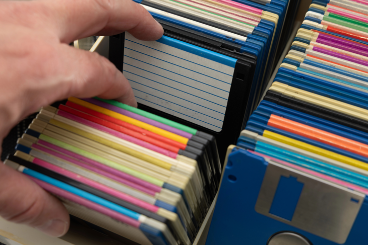 A hand flipping through rows of colorful 3.5-inch floppy disks packed into storage boxes.