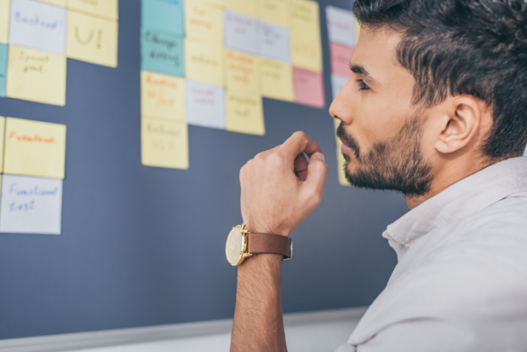 Software engineer studying a board of sticky notes while mapping out a test plan.