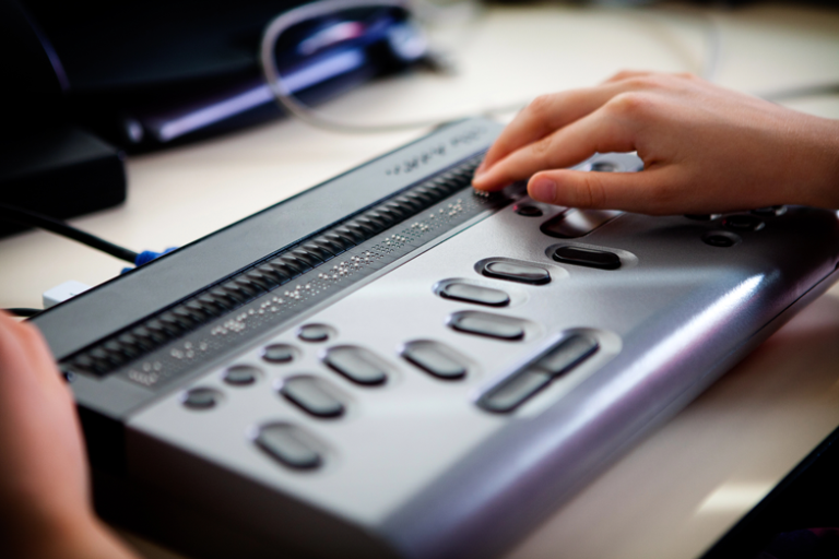 Hands using a refreshable braille display connected to a computer.